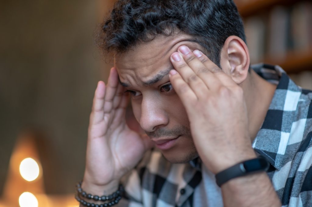 Dark-haired man in a checkered shirt having a headache